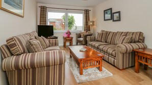 A living room with striped sofas, a wooden coffee table, a TV, and a window with curtains. - 10 Goodhope Gardens (Aberdeen)