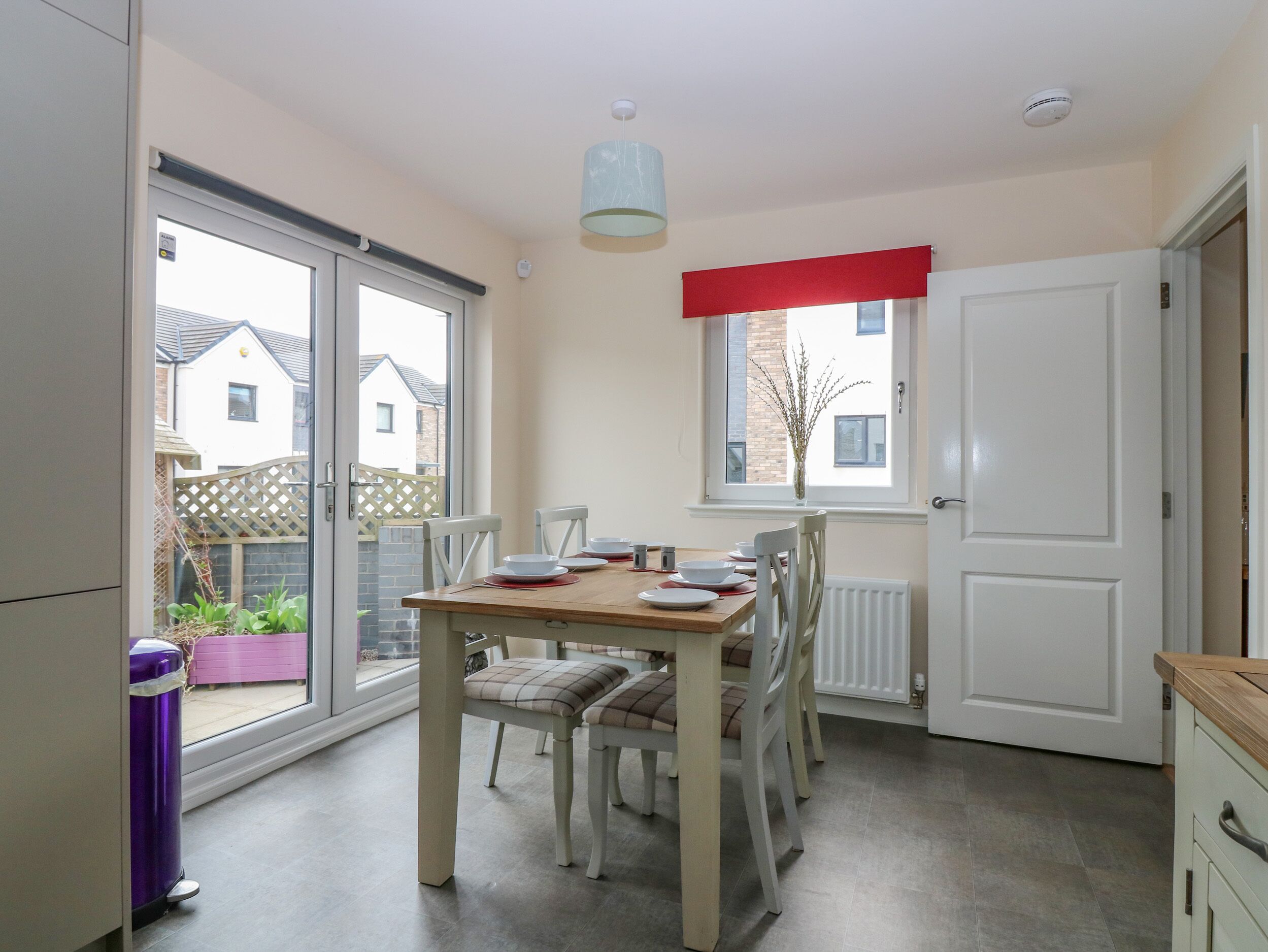 A dining area with a table set for four, a window with a red valance, and a view of a residential area.