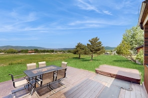 Enjoy dining or socializing on the deck with a view of the lush green field and distant hills.