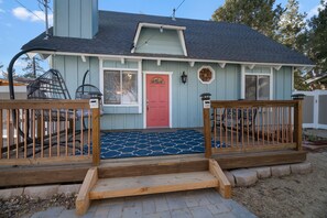 Una casa con puerta roja, fachada azul y terraza de madera con alfombra estampada en azul.