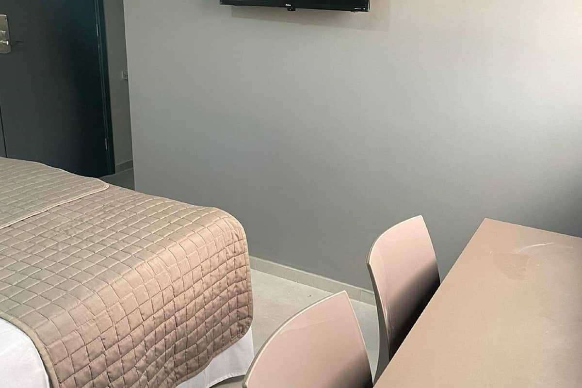 A hotel room with a bed, a table, chairs, and a flat-screen TV mounted on the wall.