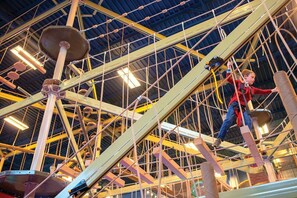 Explore the indoor climbing structure with a network of ropes and wooden beams, featuring climbing holds and platforms at various heights.