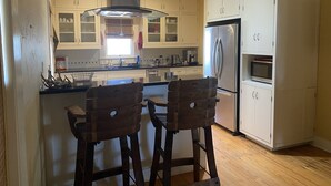 Una cocina con armarios blancos, un refrigerador de acero inoxidable, un microondas y dos taburetes de bar de madera.