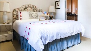 Una camera da letto con una testiera fiorata, una coperta bianca con pois rosa, un comodino in legno con una lampada e un tavolino anch'esso illuminato.
