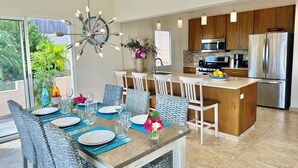 Una cocina moderna con electrodomésticos de acero inoxidable, un comedor con sillas de mimbre y un amplio ventanal con vistas a la vegetación.