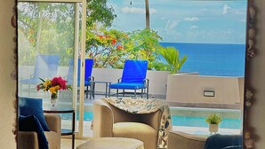 Habitación soleada con vistas al mar, que incluye un sofá, sillas y una pequeña mesa.