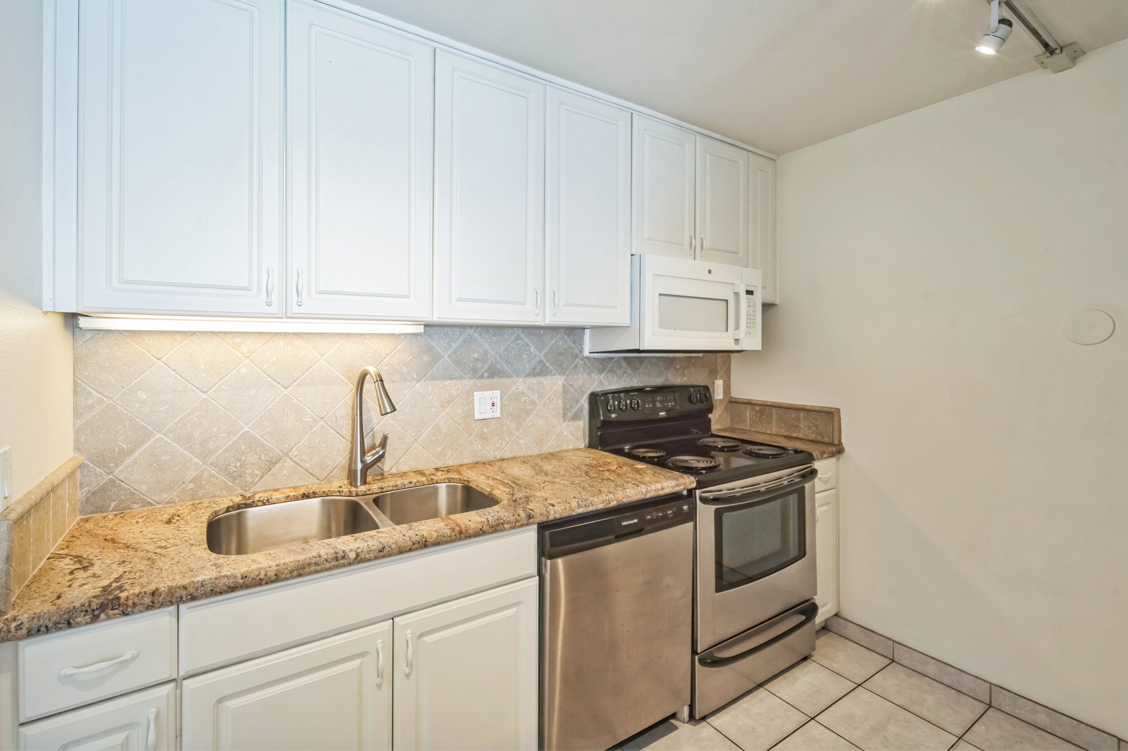 A kitchen with white cabinets, a stainless steel sink, a microwave, a stove, and a dishwasher.
