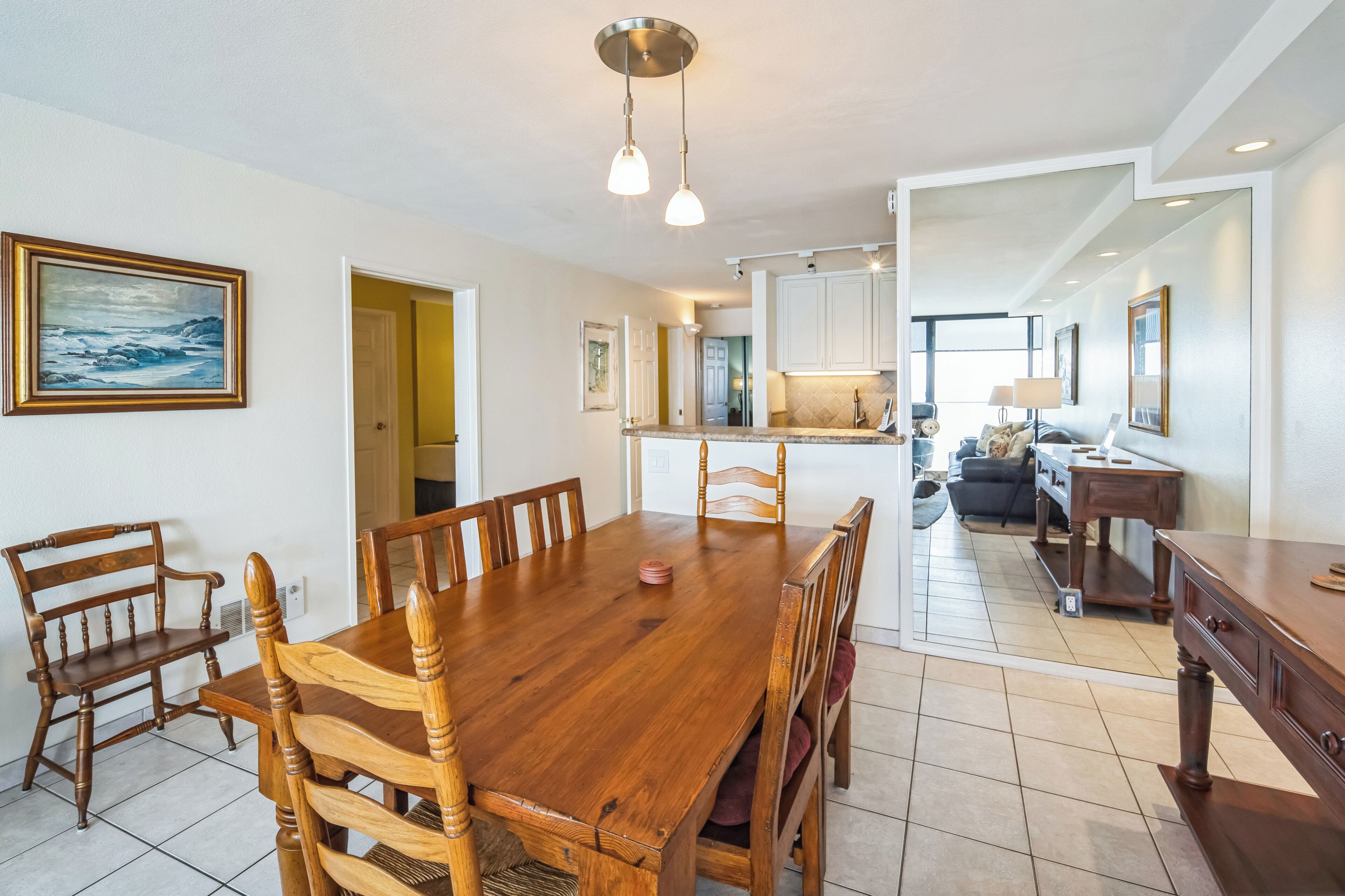 A spacious dining area with a wooden table and chairs, a kitchen in the background, and a painting on the wall.