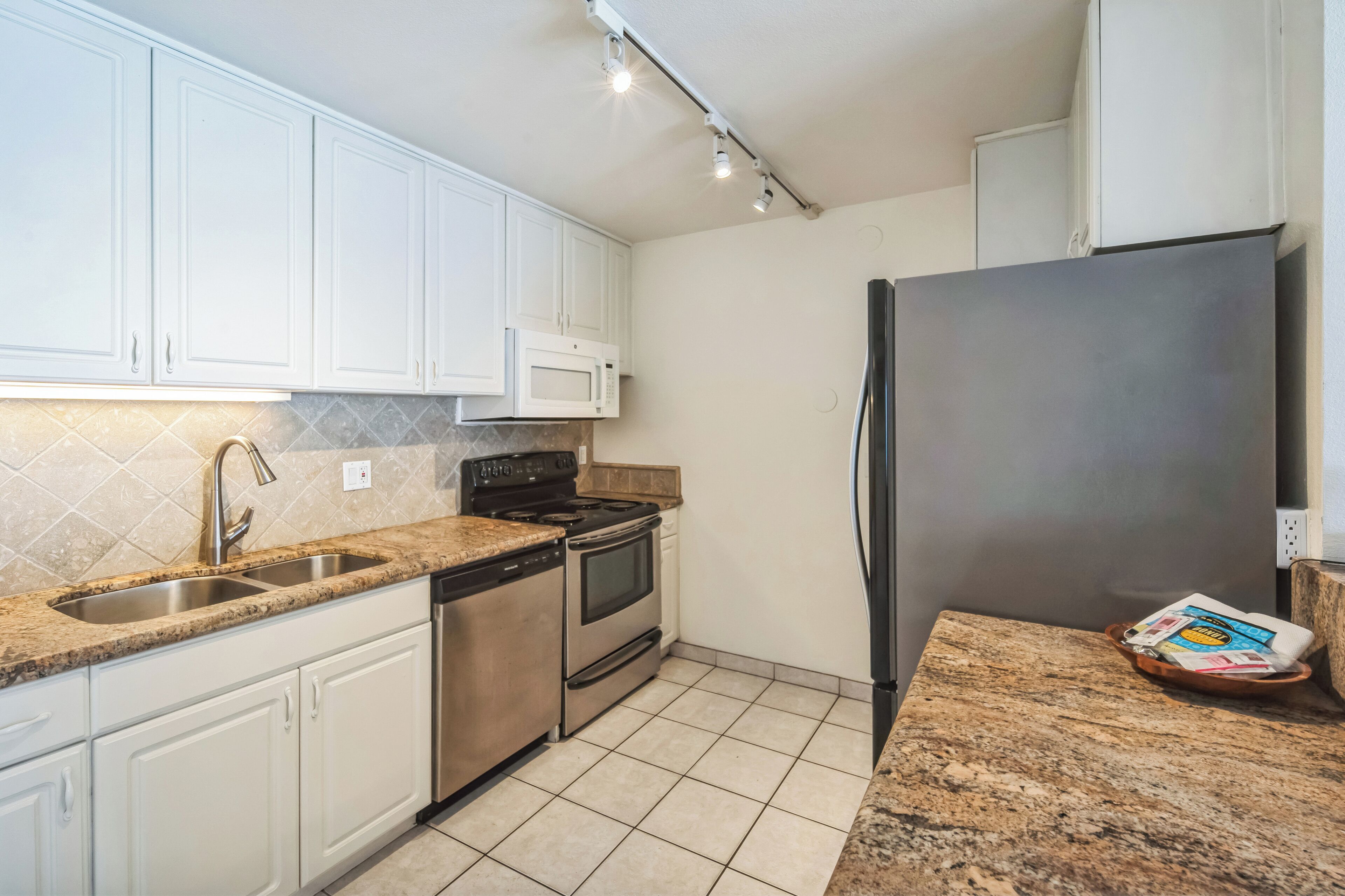 A kitchen with white cabinets, stainless steel appliances, a granite countertop, and a tiled floor.