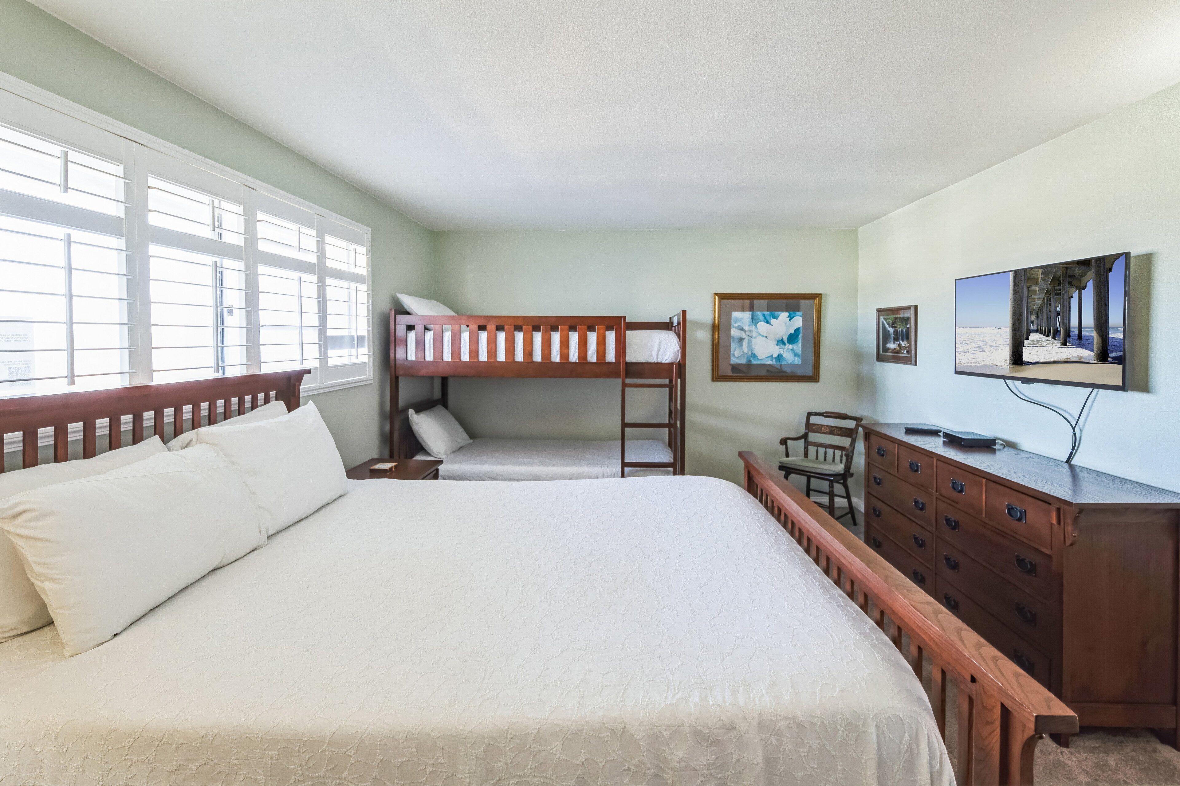 Una habitación con una cama grande, una cama individual apilable, un aparador de madera, un escritorio y un televisor.
