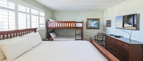 Una habitación con una cama grande, una cama individual apilable, un aparador de madera, un escritorio y un televisor.