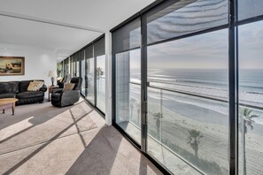 A spacious living room with a large sliding glass door leading to a balcony overlooking the ocean. - Capri by the Sea 505 | Ocean View | Full Kitchen | Private Bedroom | Beach Access | On the Boardwalk (San Diego)