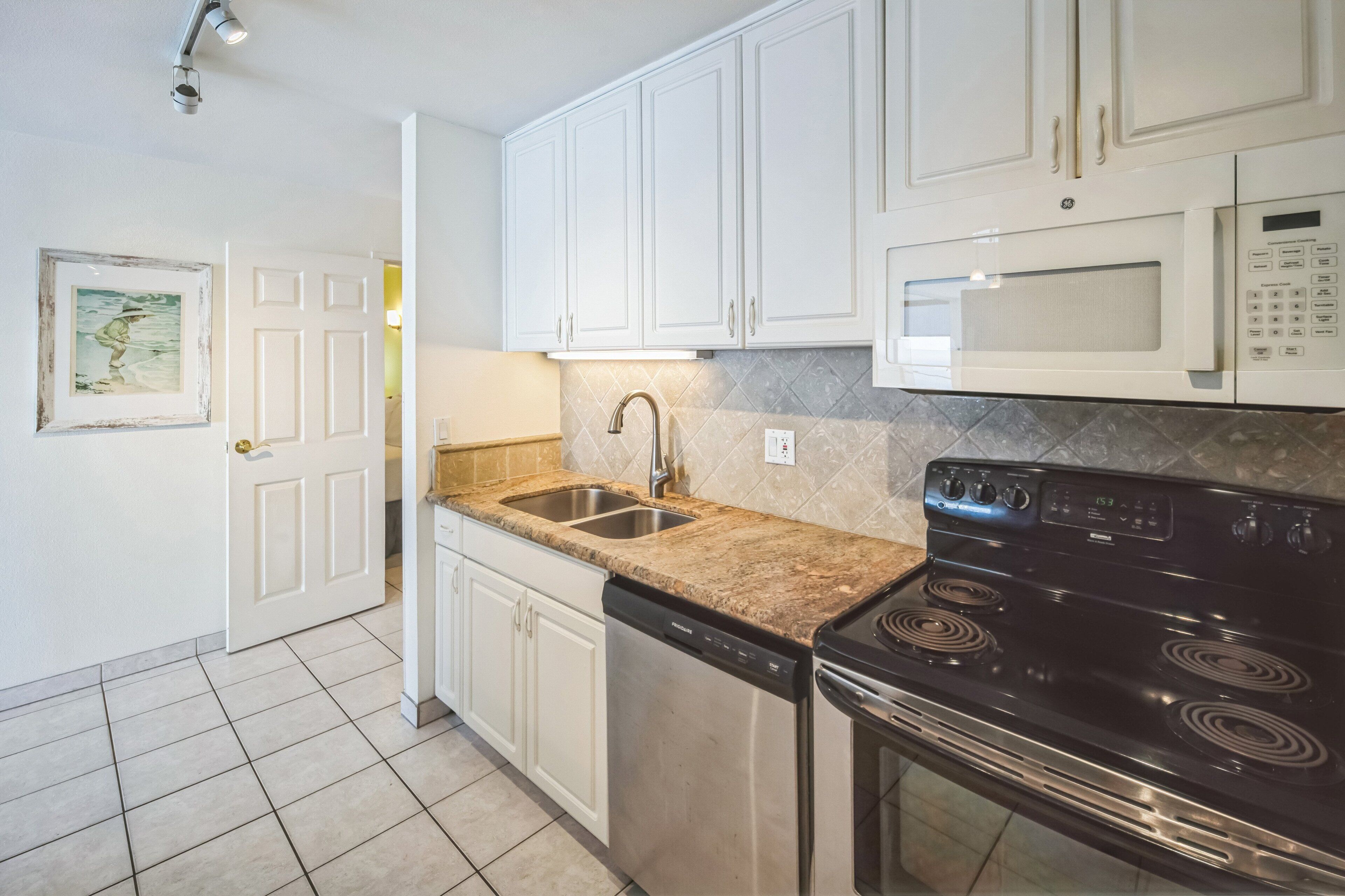 A kitchen with white cabinets, a double sink, a dishwasher, a stove, and a microwave.