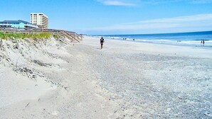 A beach with a person walking, a building on the left, and the ocean in the background. - ❤️Amazing Round House - Easy Self Check-In, Just Steps to Beach! (Carolina Beach)
