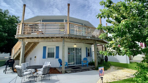 A two-story wooden building with a balcony, outdoor seating, and a welcome sign.