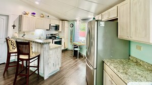 A kitchen with white cabinets, a microwave, a refrigerator, and a wooden island with bar stools. - ❤️Amazing Round House - Easy Self Check-In, Just Steps to Beach! (Carolina Beach)