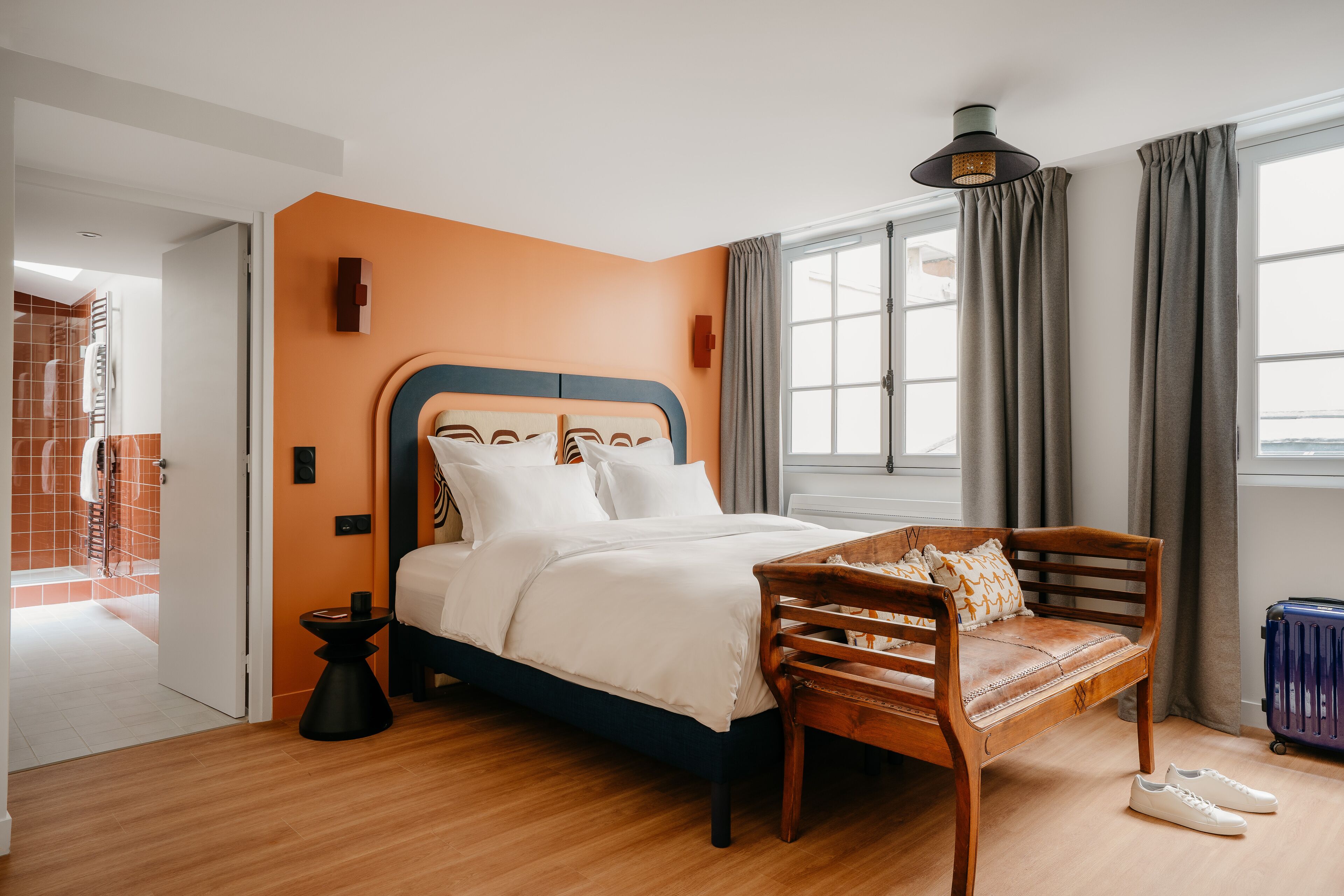Een slaapkamer met een bed, een houten bankje, een koffer en een raam met gordijnen.