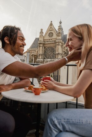 Two people sitting at a table with a view of a historic building in the background. - Edgar Suites Louvre - Jour (Paris)