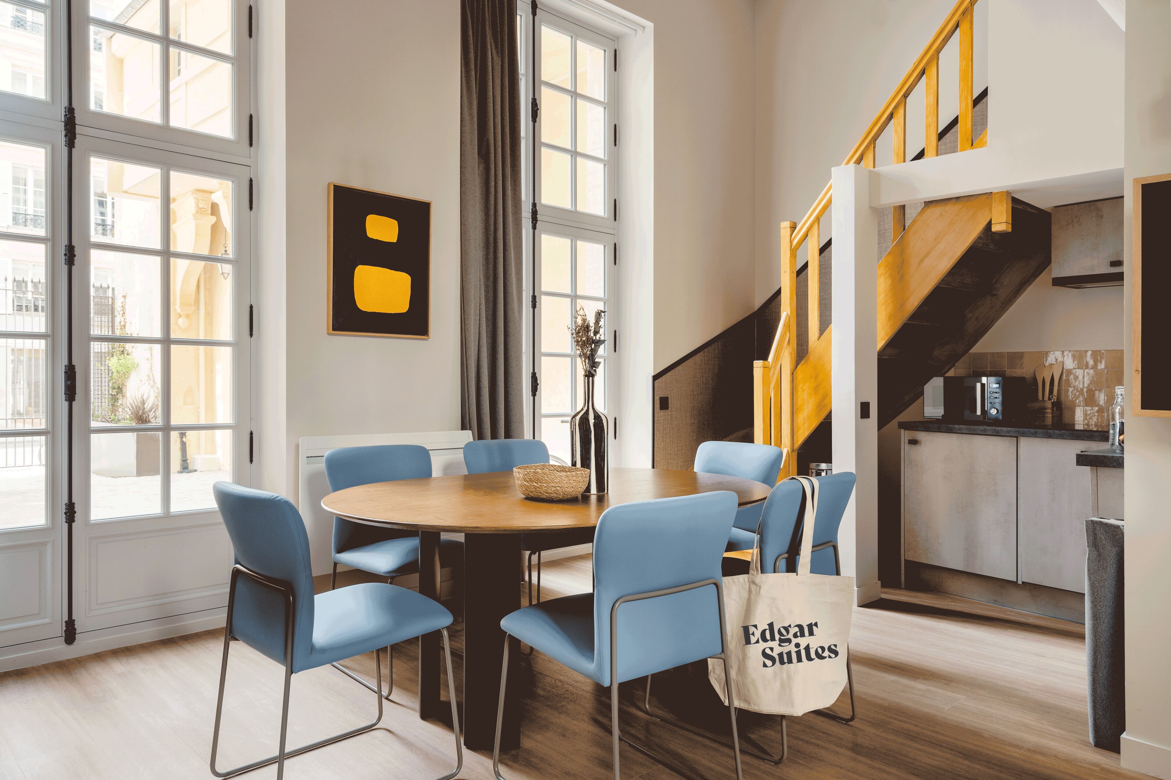 A modern hotel room with a dining area, a staircase, and a view of the city.