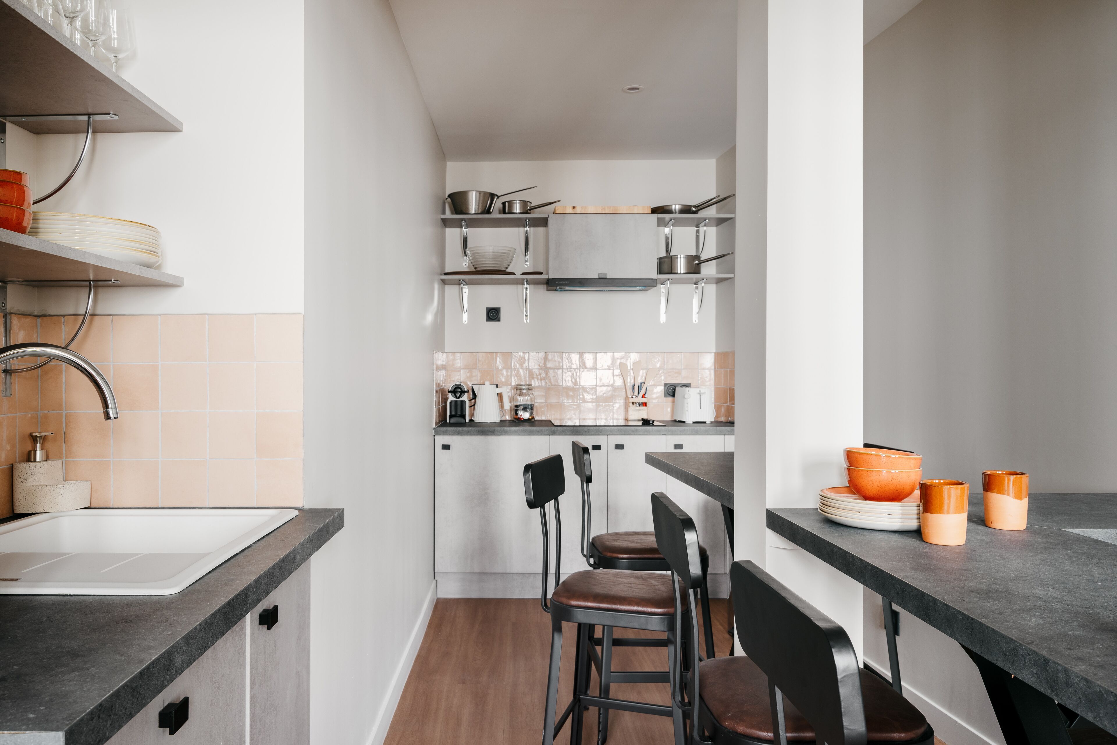 A modern kitchen with a built-in sink, a countertop with a coffee machine, and a dining area with bar stools.