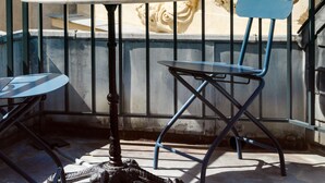 Una terraza con mesa y sillas, una barandilla decorativa y fachada de edificio con intrincados adornos.