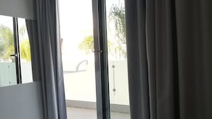 A hotel room with a large sliding glass door leading to a balcony, a bed with a patterned bedspread, and a tiled floor. - Hotel Presidente (Porto Cesareo)