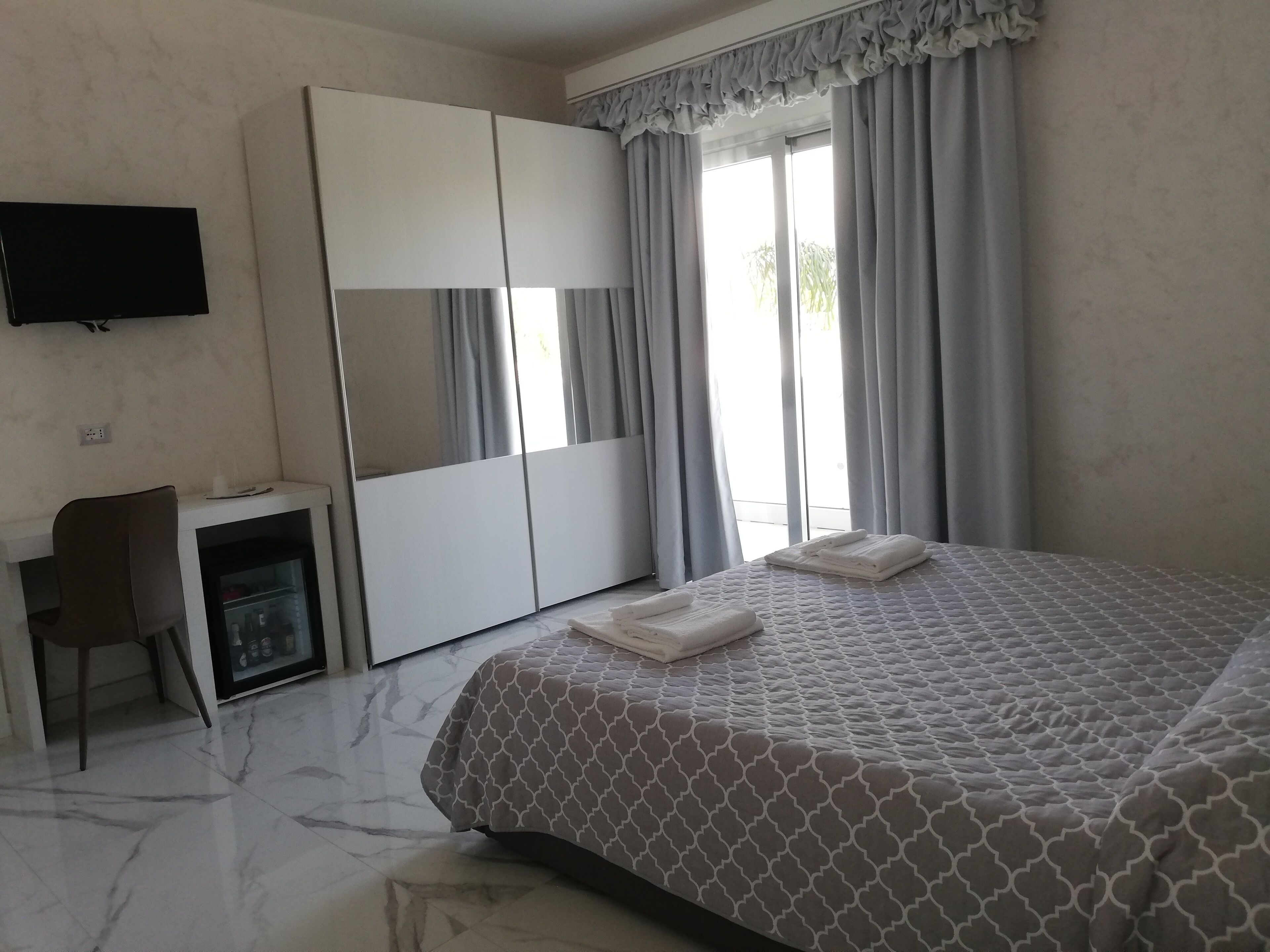A hotel room with a bed, a desk, a wardrobe, and a TV on the wall.