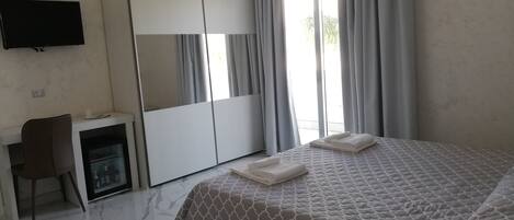 A hotel room with a bed, a desk, a wardrobe, and a TV on the wall.