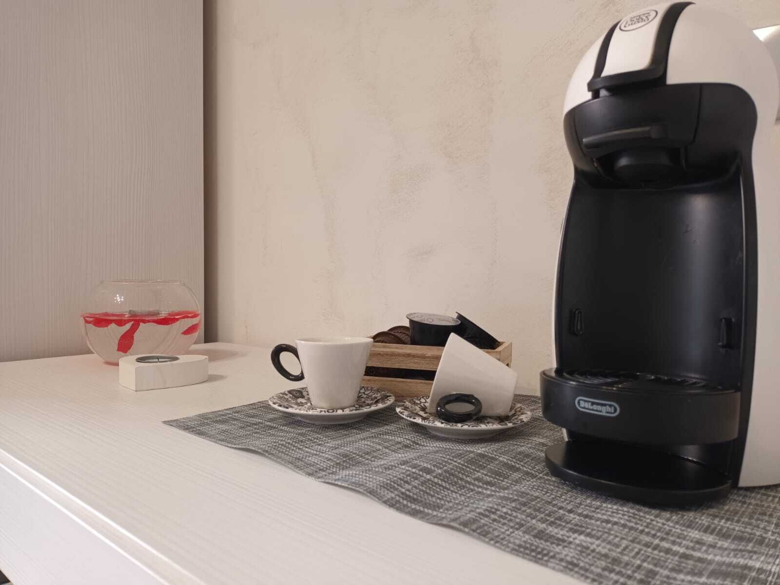 A coffee maker on a table with a cup and saucer, a tissue box, and a glass of water.