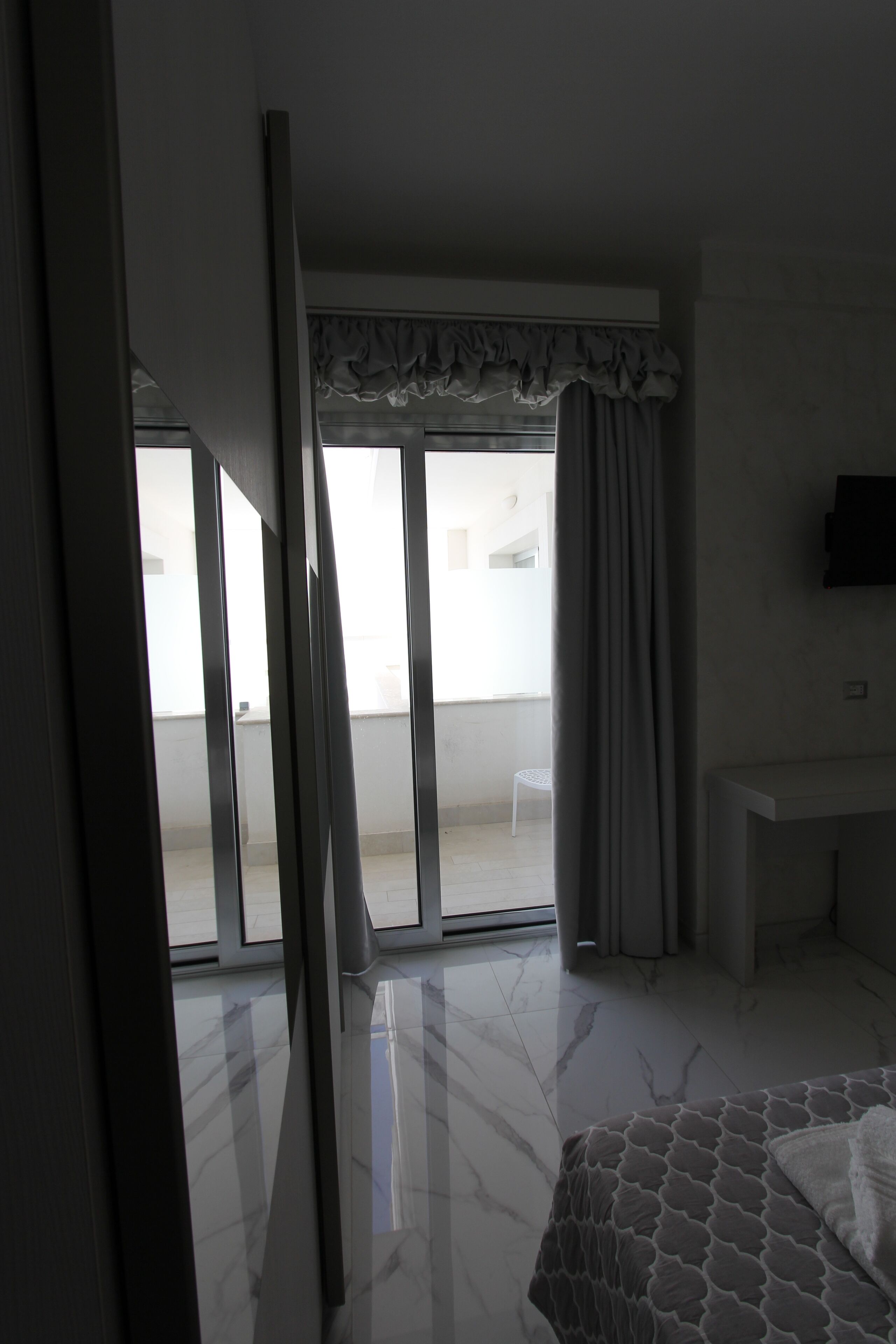Una habitación de hotel con cama, escritorio, televisor y balcón con cortinas.