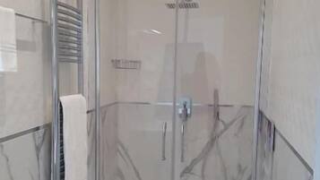 A modern bathroom with a glass-enclosed shower, a white toilet, and a marble-tiled floor.