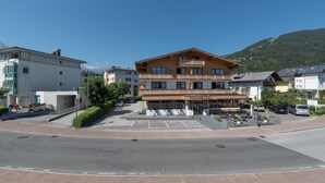 A multi-story building with a restaurant on the ground floor, a parking area, and a mountain in the background. - Apartment Kitz Thirty Nine - near AreitXpress (Zell am See)