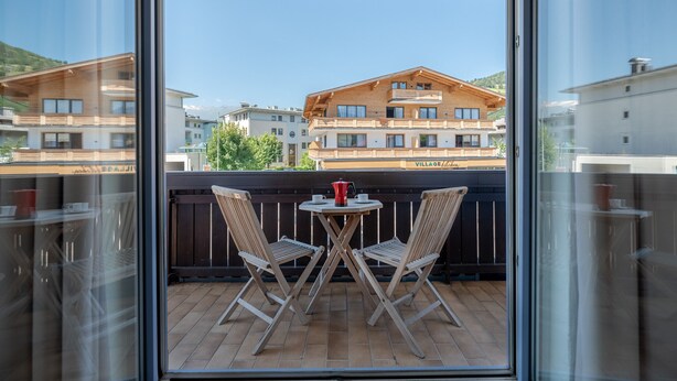 A balcony with two wooden chairs and a small table, overlooking a mountain and several buildings. - Apartment Kitz Thirty Nine - near AreitXpress (Zell am See)