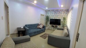 Ein modernes Wohnzimmer mit einem blauen Sofa, einem grauen Sofa und einem Flachbildfernseher, der an einer strukturierten Wand angebracht ist.