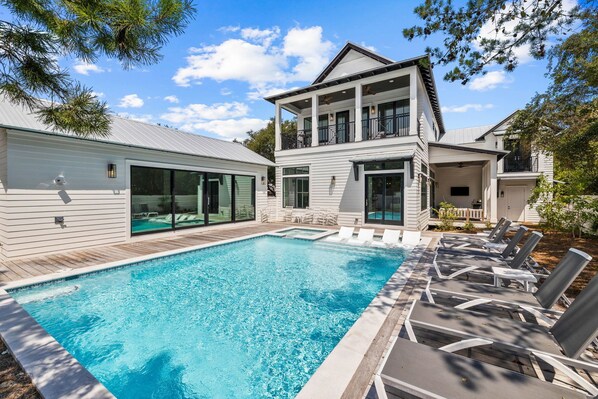 Une maison à deux étages avec une piscine et des chaises longues.