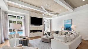A modern living room with a fireplace, a ceiling fan, a flat-screen TV, and a pool view. - Casa al Mare|Easy Beach Access|Private Pool|Golf Cart (Seagrove)