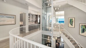 Un intérieur à plusieurs niveaux, doté d’un escalier en verre, de rampes blanches et de luminaires suspendus.