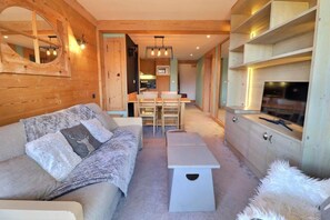 A cozy living room with a sofa, a small table, and a TV. There is a kitchen area with a dining table and chairs. - 200m from shops, 6th floor, 47m², Méribel-Mottaret (Méribel - Les Allues)