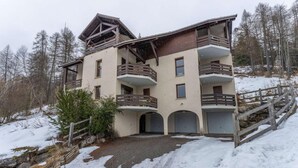 Un edificio de varios pisos con balcones, un telesilla y un paisaje nevado.