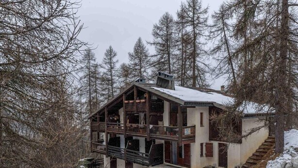 Una cabaña con balcón, una escalera y un suelo cubierto de nieve.