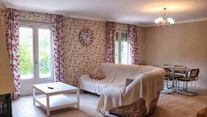 Een woonkamer met een bank, een salontafel, een eettafel met stoelen en een klok aan de muur.