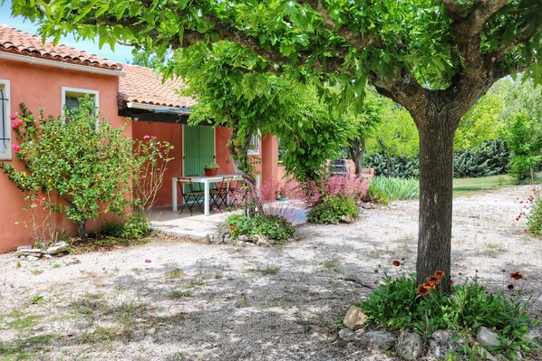 A rustic house with a tiled roof, a covered patio, and a garden with various plants and flowers.