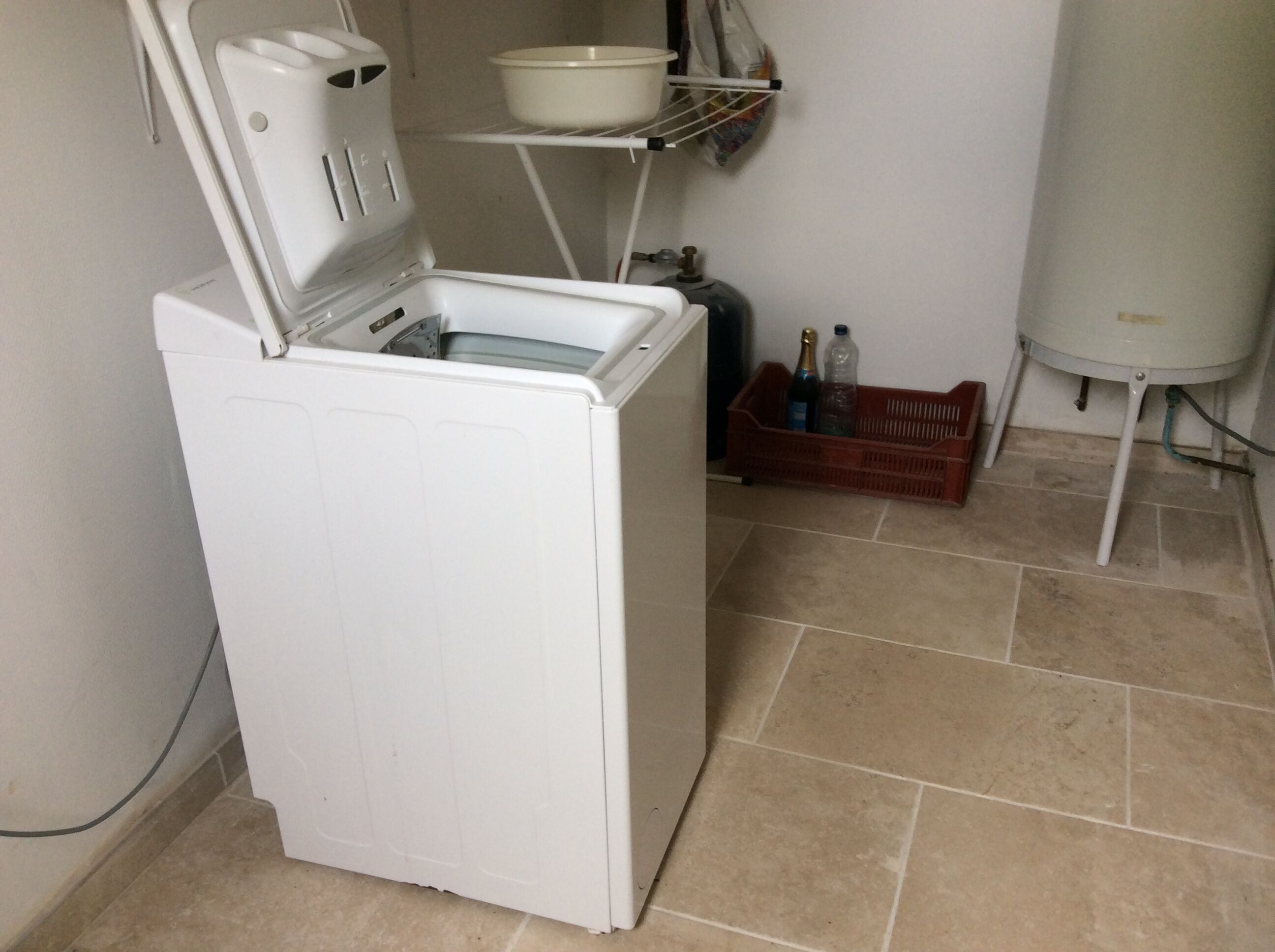 Een compacte, witte wasmachine in een kleine wasruimte met betegelde vloer.