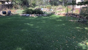 A backyard with a well-maintained lawn, a stone border, and a metal grill.