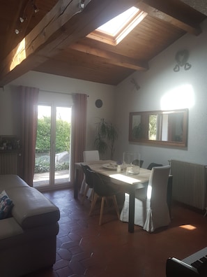 Un espace repas comprenant une table, des chaises, un canapé et une vue sur l’extérieur, accessible par une porte vitrée.