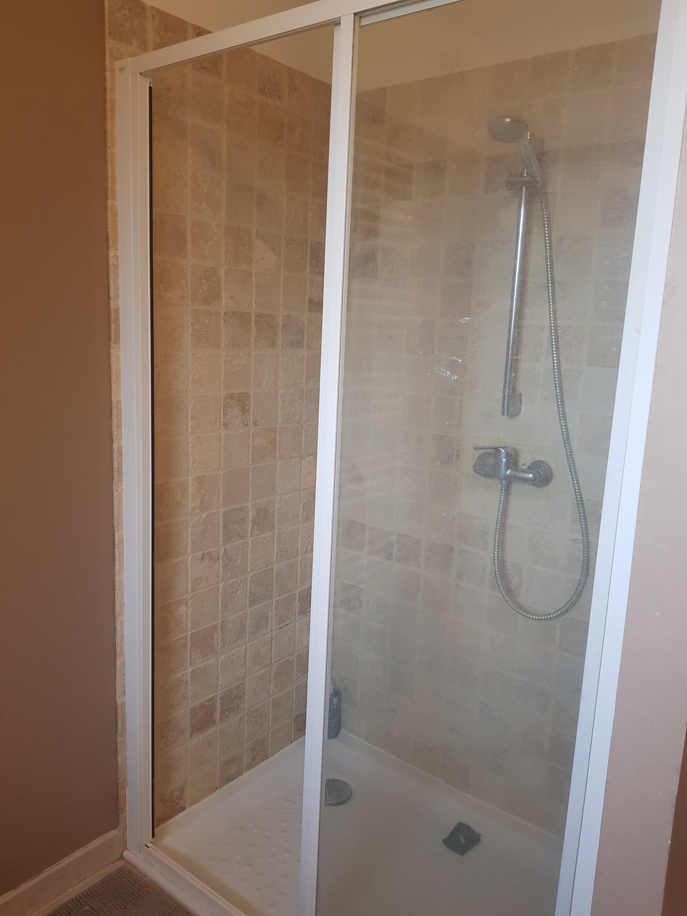 Ducha con mampara de vidrio, cabezal de ducha manual y otro fijo en la pared.