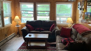 A cozy living room with wooden walls and ceiling, two couches with red and black cushions, a coffee table, and a patterned rug. - Updated Camp- 5 min  to Old Forge, 1st Lake views (Old Forge)