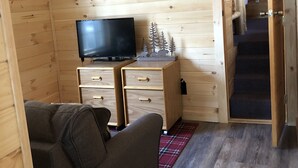A wooden cabin interior with a television on a dresser, a sofa, and a staircase leading to an upper level. - Updated Camp- 5 min  to Old Forge, 1st Lake views (Old Forge)
