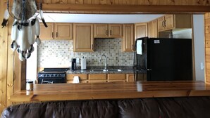 A kitchen with wooden cabinets, a black refrigerator, a stove, and a coffee maker. - Updated Camp- 5 min  to Old Forge, 1st Lake views (Old Forge)
