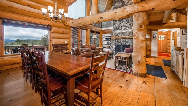 A log cabin interior with a dining area, fireplace, and large windows offering views. - Luxury Log Cabin-Windham Mountain.  Amazing sunsets, large lawn, deck, fireplace (Windham)